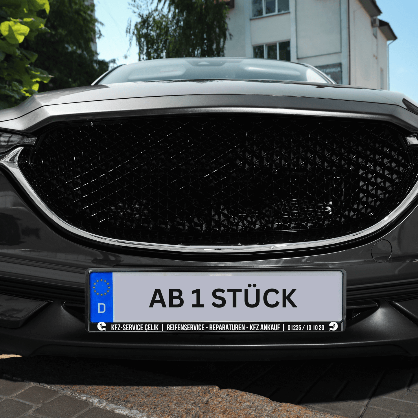 Personalisierter Kennzeichenhalter mit individuellem Text 'AB 1 STÜCK' an einem Fahrzeug.
