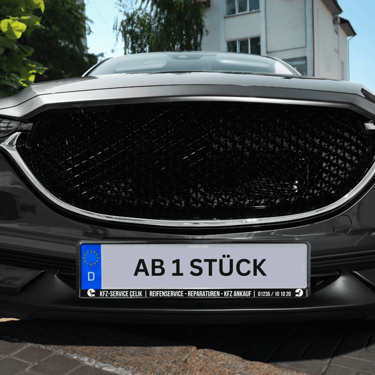 Personalisierter Kennzeichenhalter mit individuellem Text 'AB 1 STÜCK' an einem Fahrzeug.